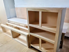 Unfinished custom wood cabinets and shelving units in a home workshop being prepared for installation.
