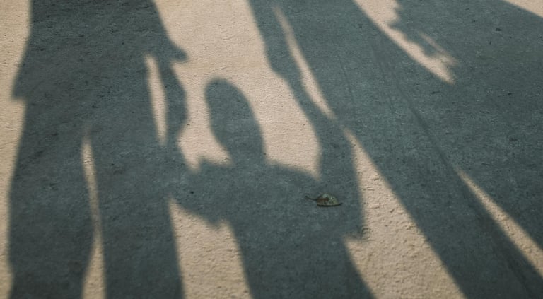Schaduw van twee volwassenen met kind ertussen: verbinding en uitsluiting.