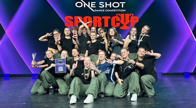 A hip-hop dance crew posing on stage with a 2nd place trophy at the One Shot Dance Competition Sport Cup.