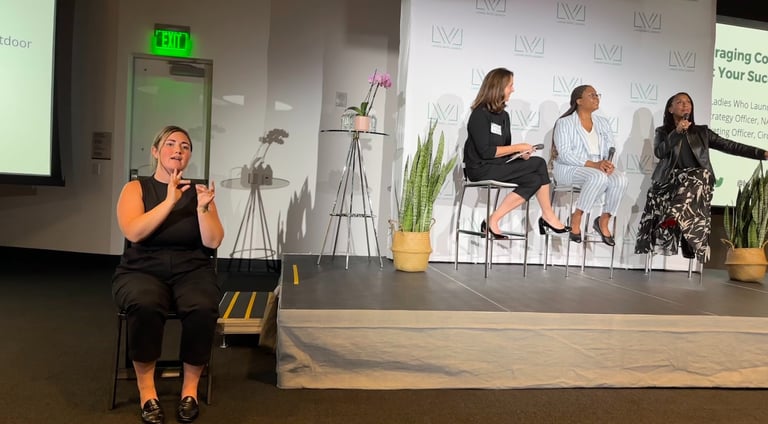 a stage with three business professionals, and a sign language interpreter to the side