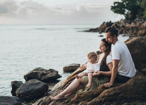 Una familia feliz con un niño pequeño sentada sobre rocas marinas en una playa