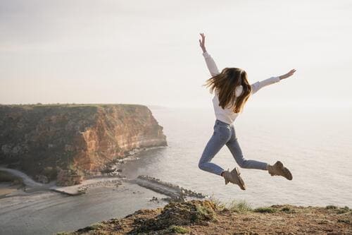Una mujer feliz saltando en el aire en un acantilado pintoresco con vistas al océano al atardecer