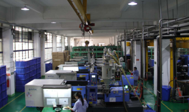 Industrial factory floor featuring rows of plastic injection molding machines and blue storage bins.