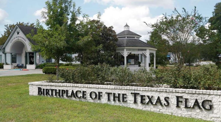 Birthplace of the Texas Flag monument sign in Montgomery, Texas, with a white gazebo and park landscaping.
