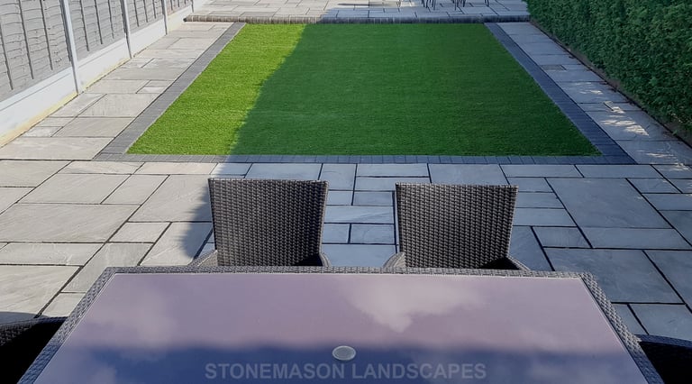 Fully paved grey sandstone patio with charcoal edging bocks and artificial grass lawn
