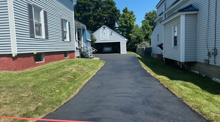 Freshly paved black asphalt driveway between two residential houses leading to a detached garage.