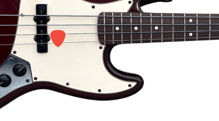 Close-up of a sunburst electric bass guitar with a red plectrum tucked into the strings.