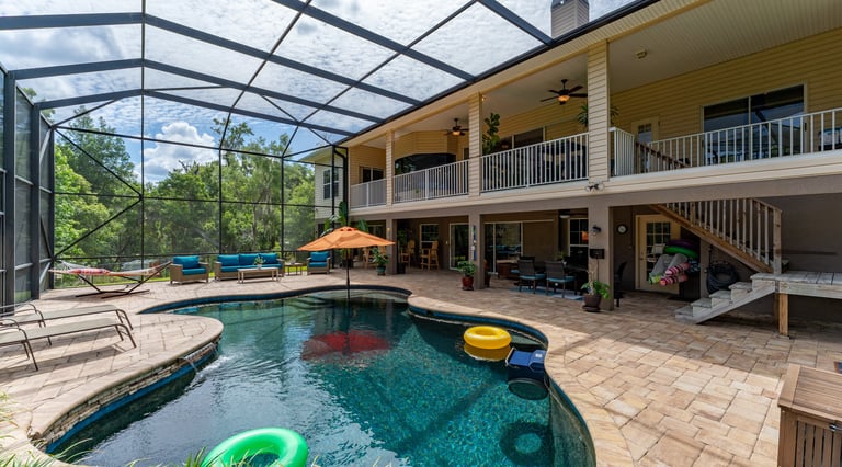 Luxury backyard swimming pool with a screen enclosure, patio furniture, and a balcony on a two-story home.