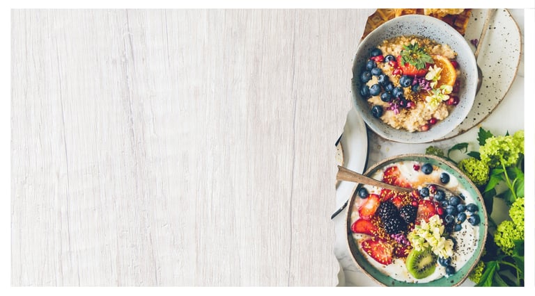 Healthy breakfast bowls with oatmeal, yogurt, fresh berries, and fruit on a rustic white wood background.