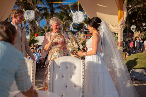 Bride and groom at an outdoor beach wedding ceremony under a canopy with palm trees.