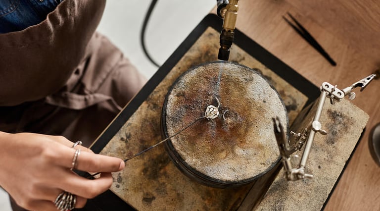 Artesano fundiendo metal con un soplete para crear una joya.