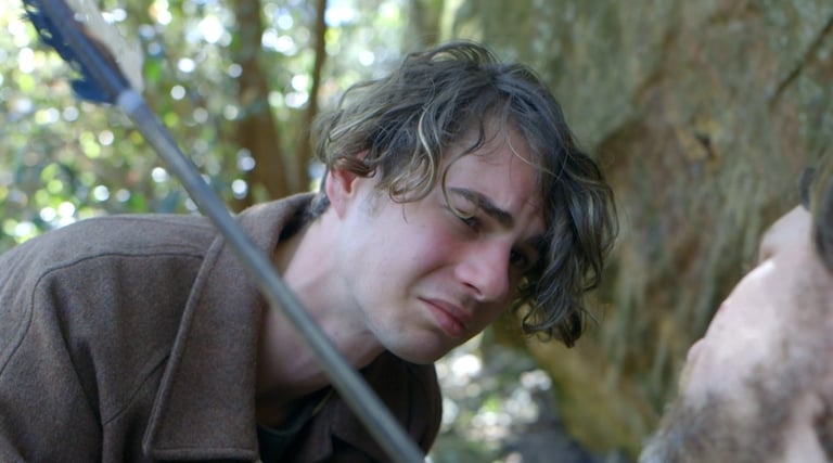 a man in a brown jacket is holding a sword