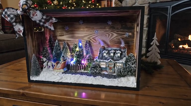 Handcrafted light-up Christmas shadow box featuring a winter village scene with Santa in a sleigh near a fireplace.