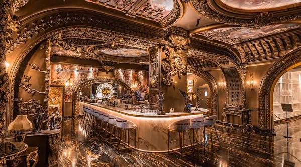 Opulent luxury bar with intricate gold carvings, marble counters, and ornate ceiling frescoes.