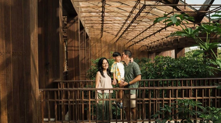 Family standing on a wooden bridge surrounded by tropical greenery during a family photography session at The Meru Sanur Bali