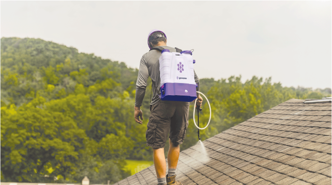 A professional roof cleaner uses a purple backpack sprayer to apply Go Nano to shingles.