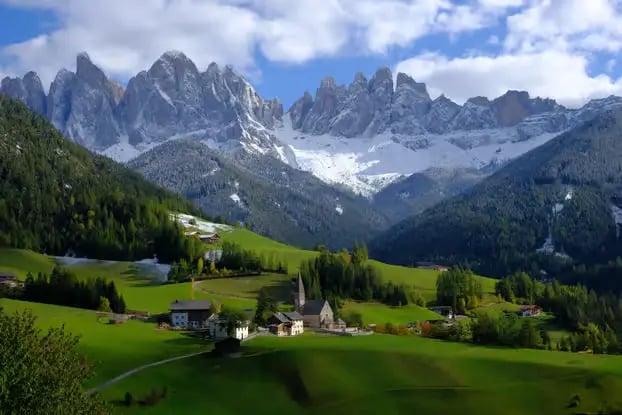 The Dolomites in spring — snow-crowned peaks rising above emerald meadows and quiet alpine villages
