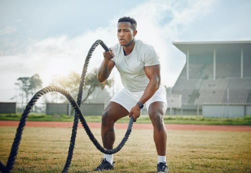 a man in white shirt and shorts using a battling rope