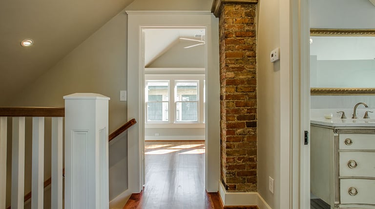 Rustic modern home hallway with exposed brick pillar, hardwood floors, and view into a bright bedroom.