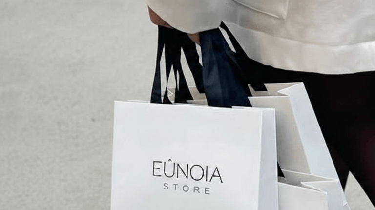 Una persona camina mientras lleva bolsas de compras de lujo blancas de Eunoia Store con asas negras.