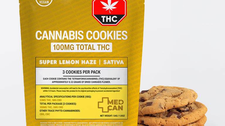 A yellow package of Super Lemon Haze Sativa Cannabis Cookies containing 100mg THC next to a stack of chocolate chip cookies.
