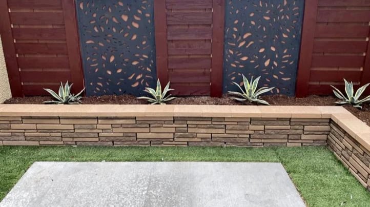 Small decorative retaining wall made of concrete blocks surrounding a garden bed in a backyard patio