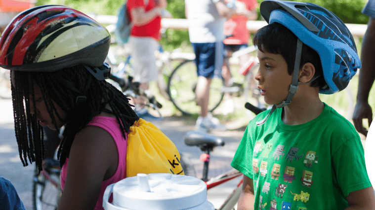 Two kids standing together wearing helmets