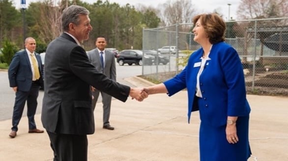 a man and woman shaking hands in front of a fence
