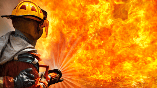 Um bombeiro combate um grande incêndio com uma mangueira, exemplificando uma crise.