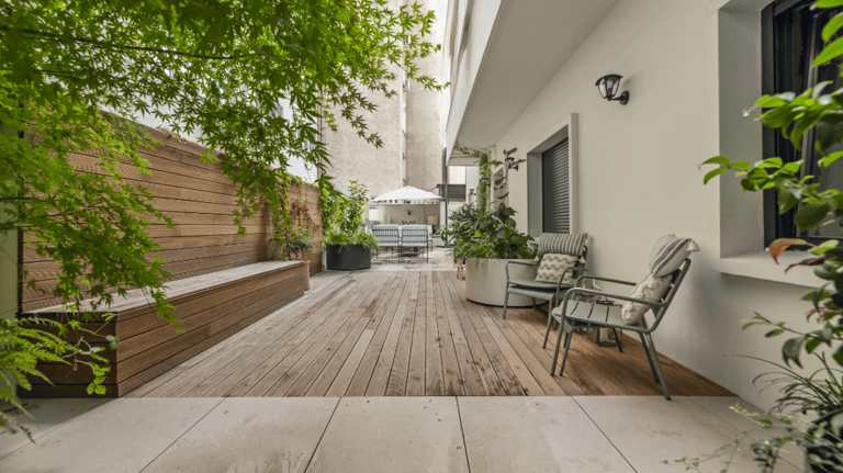 Espacio del jardín con suelo de gres estilo madera, fachada blanca y muro recubierto con madera.