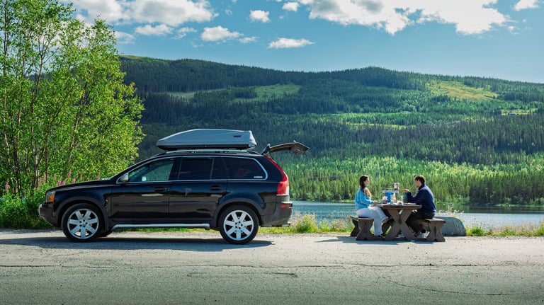 Scenic travel photograph of a couple having a picnic lunch by a lake, backed by forested mountains.