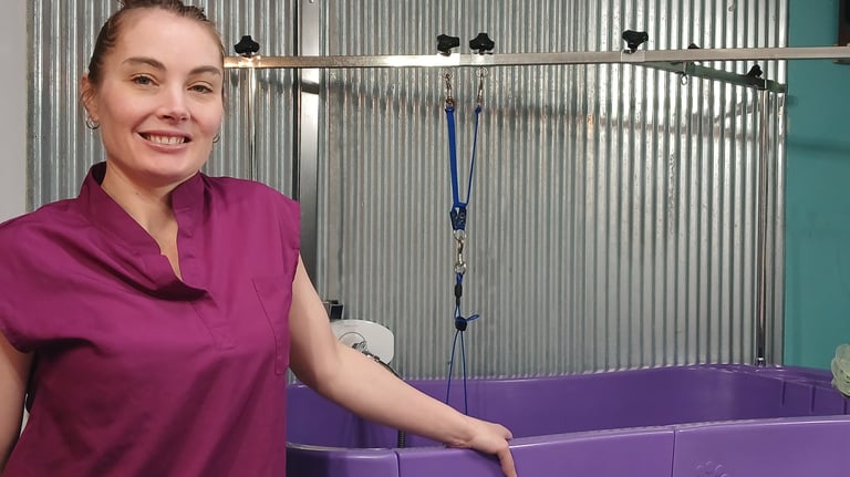 a dog groomer in a purple shirt is standing in front of a tub