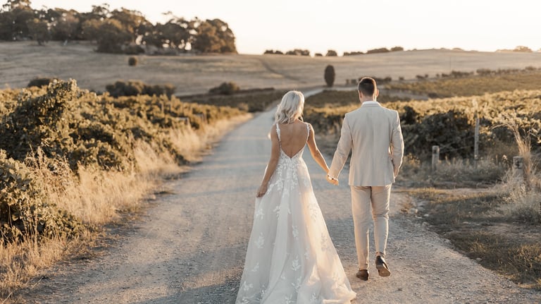 a bride and groom walking down a dirt road during sunset at Coriole Winery