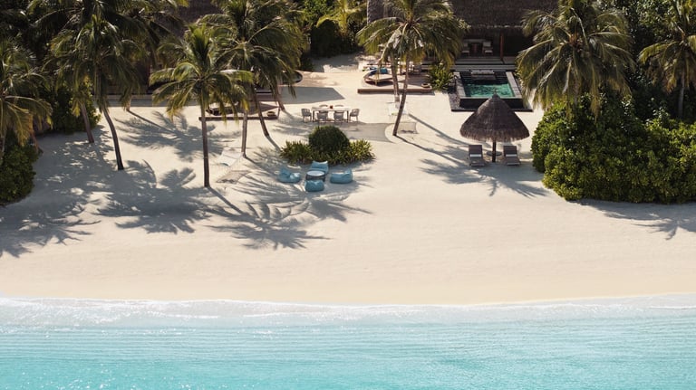 a beach with a beach chair and palm trees, One and Only Reethi Rah