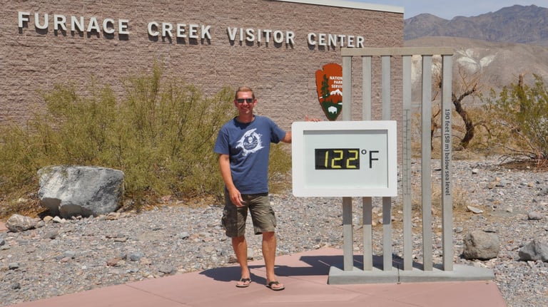 a man standing in front of a sign that says furnace furnace creek, death valley