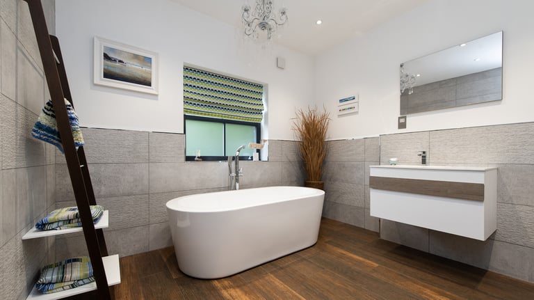 A luxury bathroom with wooden floors and grey tiles. A freestanding bath is the main feature.