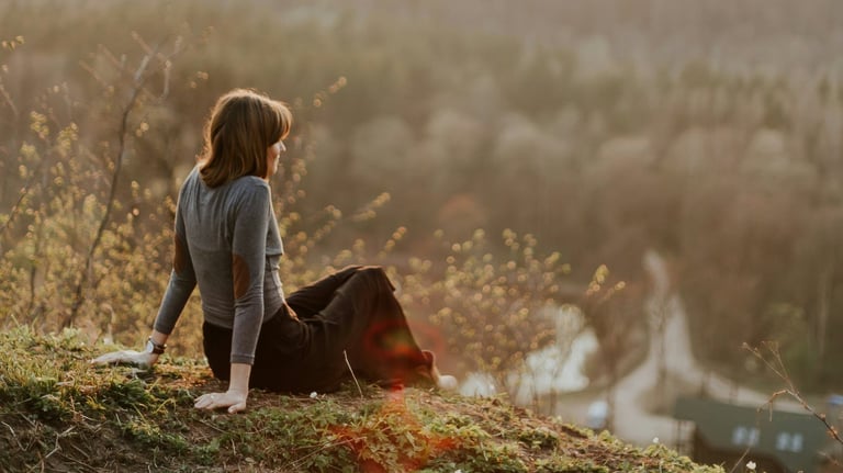 a woman sitting on a hill with a dog