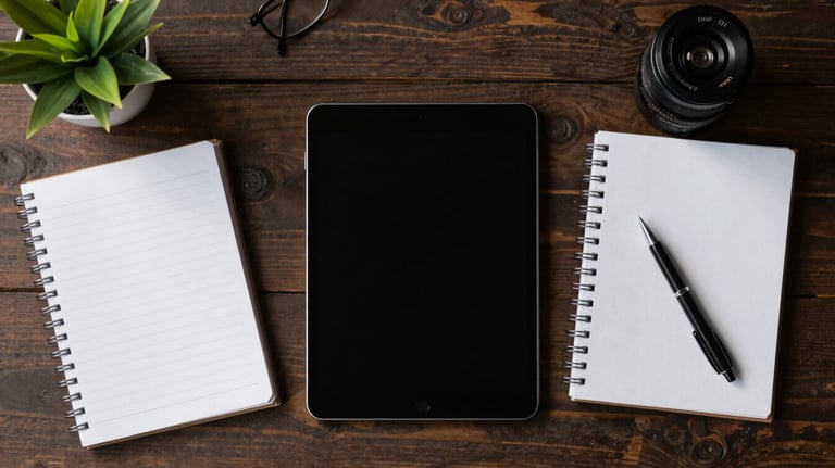 A top-down view of a stylish Latin American workspace with a tablet, a clean notebook, and a small plant, illustrating organization and modern business management.