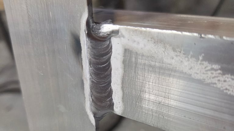 Close-up of an aluminum weld joint on aluminum square tube angle in a metal fabrication workshop.