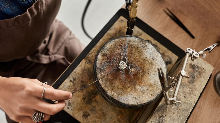 Un joyero usa un soplete para soldar un anillo de plata en un banco de trabajo dentro de un taller