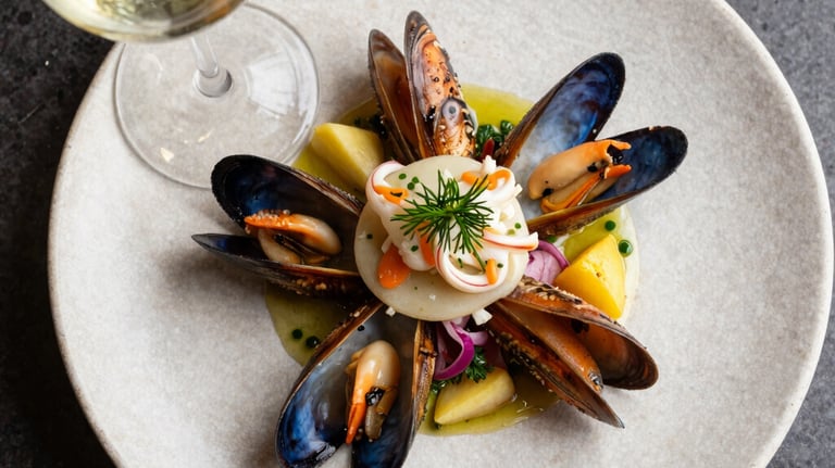 A top-down shot of a gourmet seafood dish paired with a glass of crisp white wine. Modern Spanish plating style on a stone-textured plate. Natural, bright lighting.