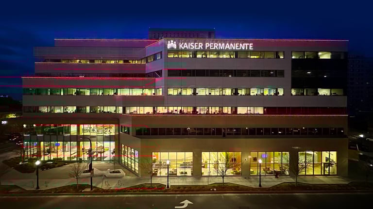 Night view of a Kaiser Permanente medical office building with glowing signs and red decorative lighting.