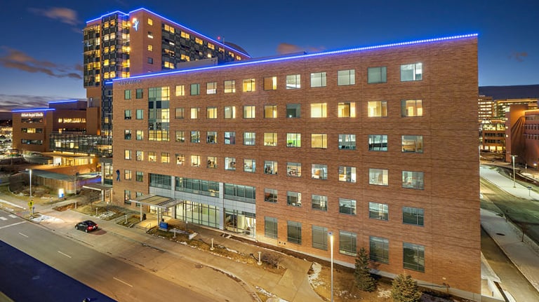 Modern brick hospital building exterior with blue LED lighting at night and glowing windows.