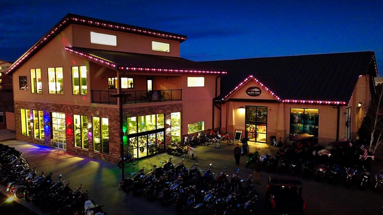 Motorcycle dealership showroom at night with rows of bikes and colorful holiday lights.