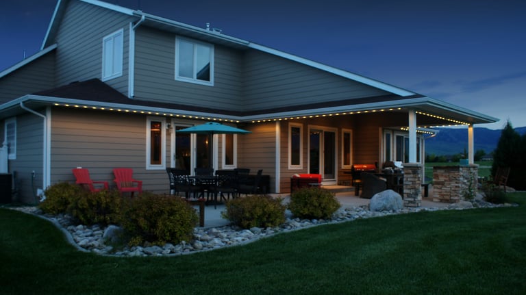 Luxury home patio with outdoor lighting, dining furniture, and stone landscaping at dusk.
