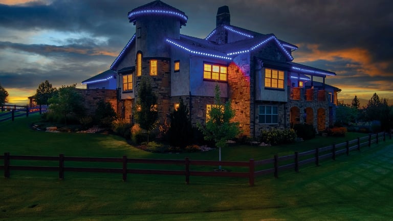 Luxury estate with blue LED holiday roof lighting and glowing windows during a dramatic sunset.