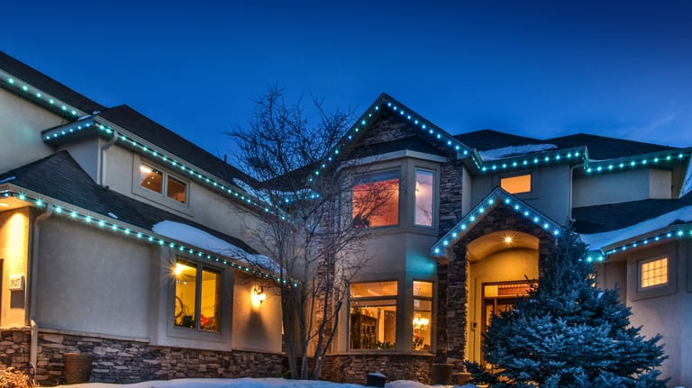 Luxury home exterior with festive blue LED Christmas lights on the roofline during winter twilight.