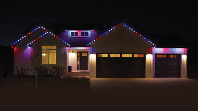 Modern white house at night with festive red, white, and blue permanent LED holiday roof lighting.