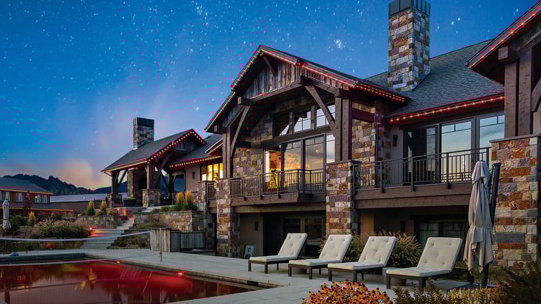 Luxury mountain estate with stone exterior, pool, and lounge chairs under a starry night sky.