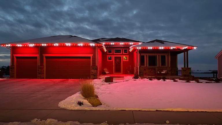 Modern ranch home featuring red and white LED roofline holiday lights on a snowy winter night.
